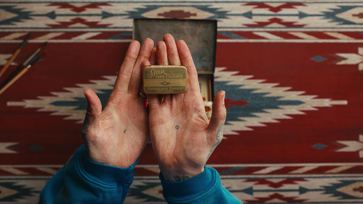 A small decorative tin holding nib cleaning tools and small stamps