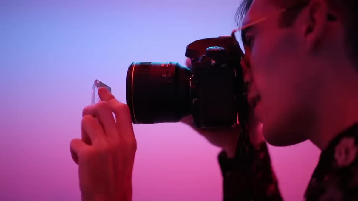 Peter holding a glass prism up to the camera lens in the neon room