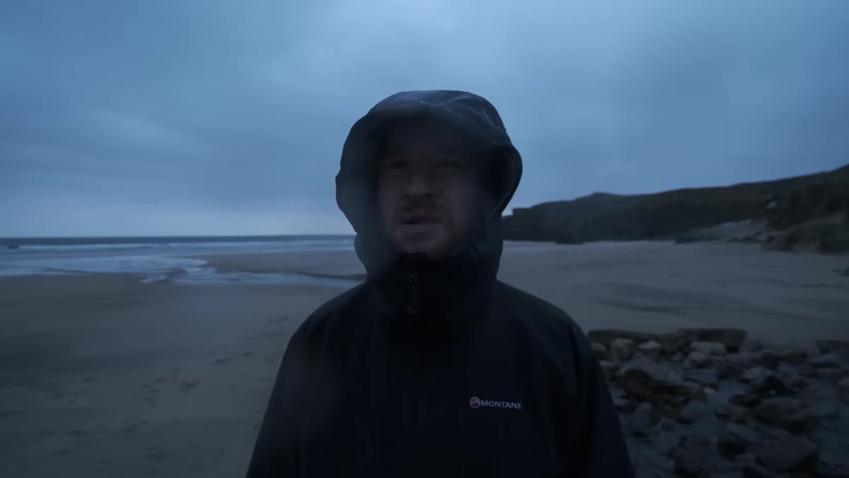 Thomas standing on a beach in heavy rain, scouting